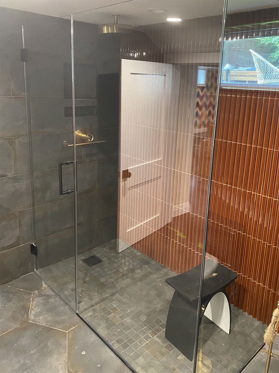A bathroom with a glass shower door and a bench