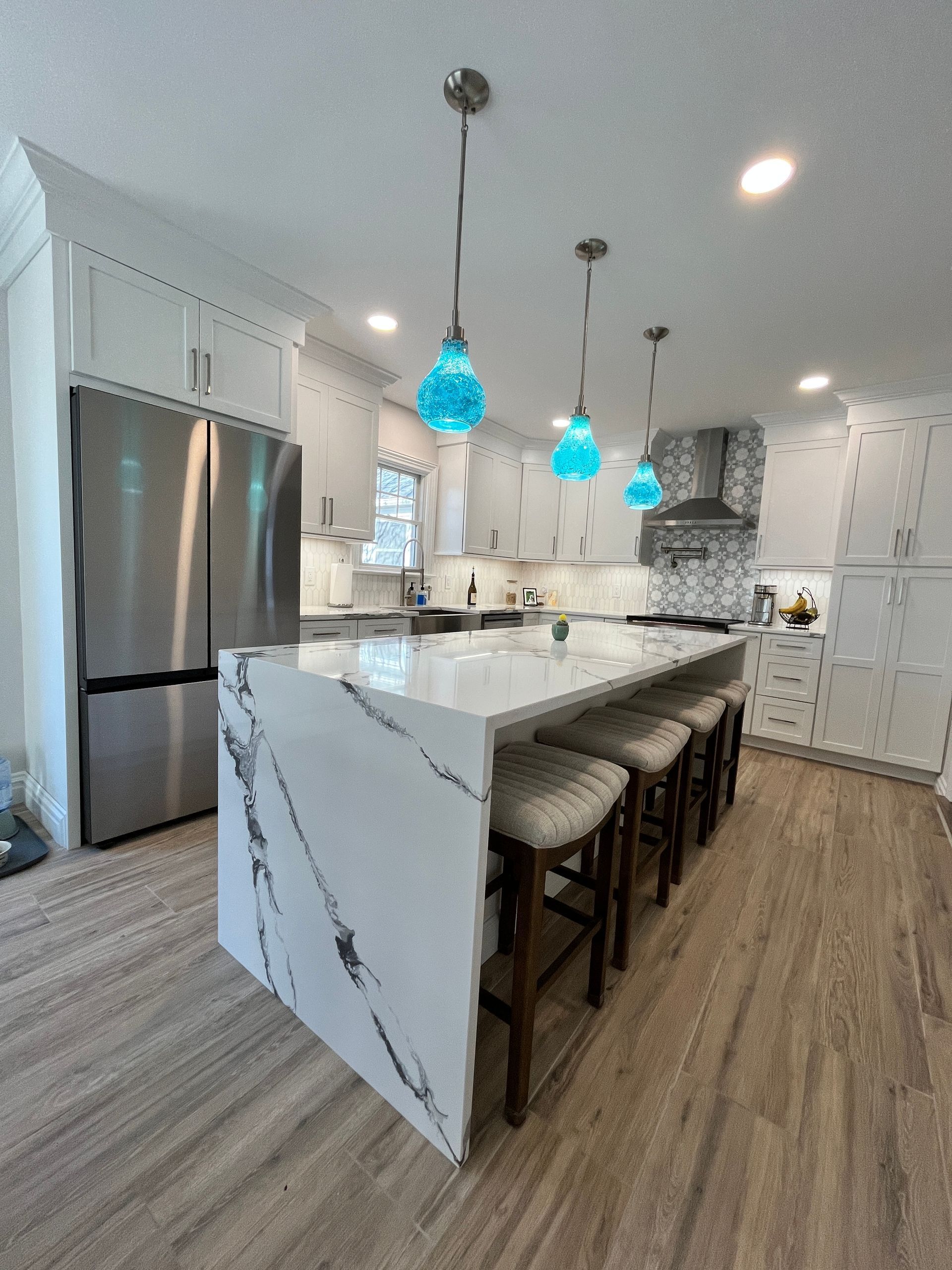 A kitchen with white cabinets , stainless steel appliances , a large island and blue pendant lights.