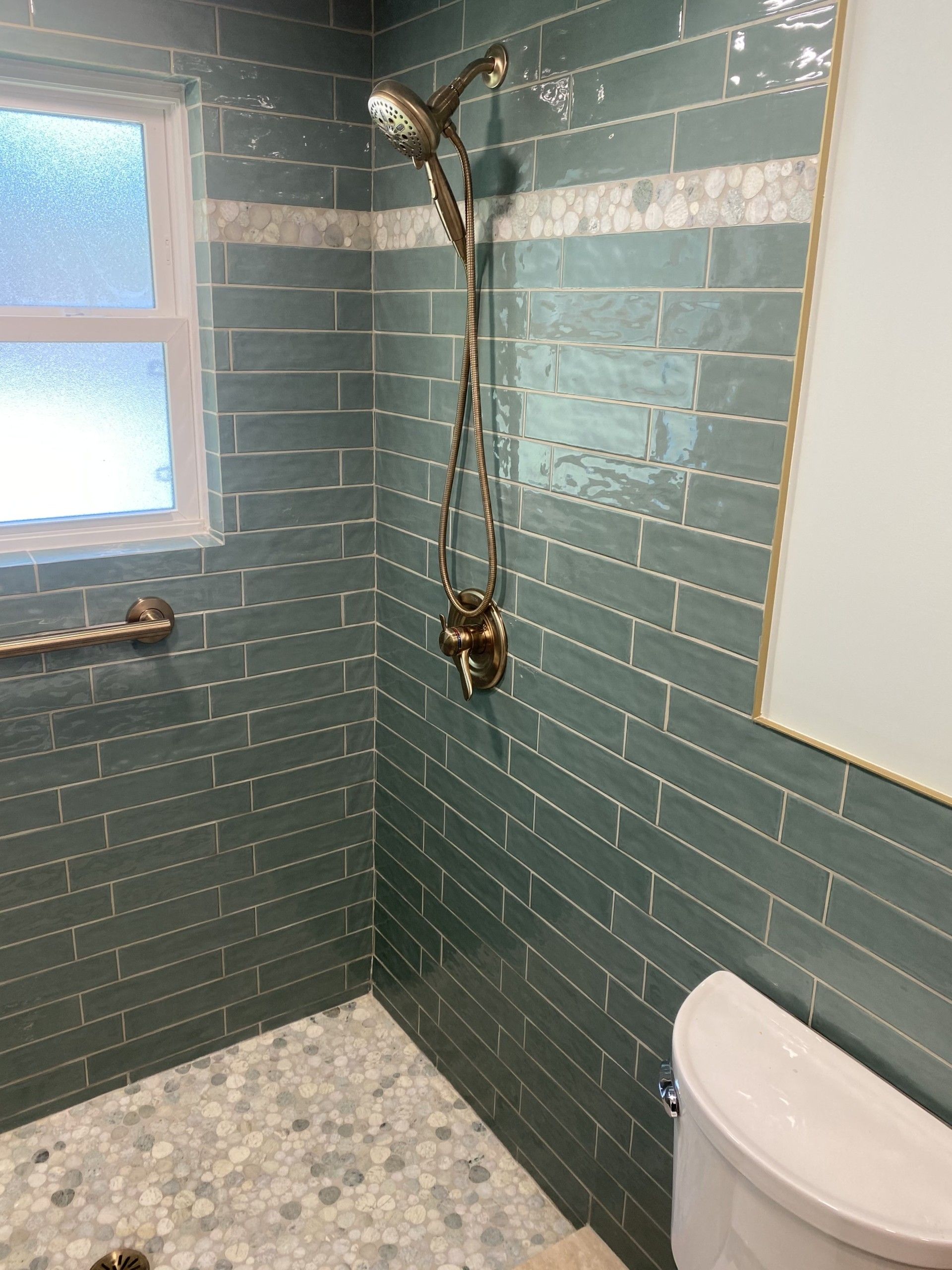 A bathroom with green tiles , a toilet , and a shower.