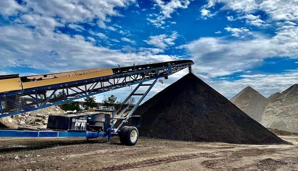 A conveyor belt is carrying a large pile of dirt.