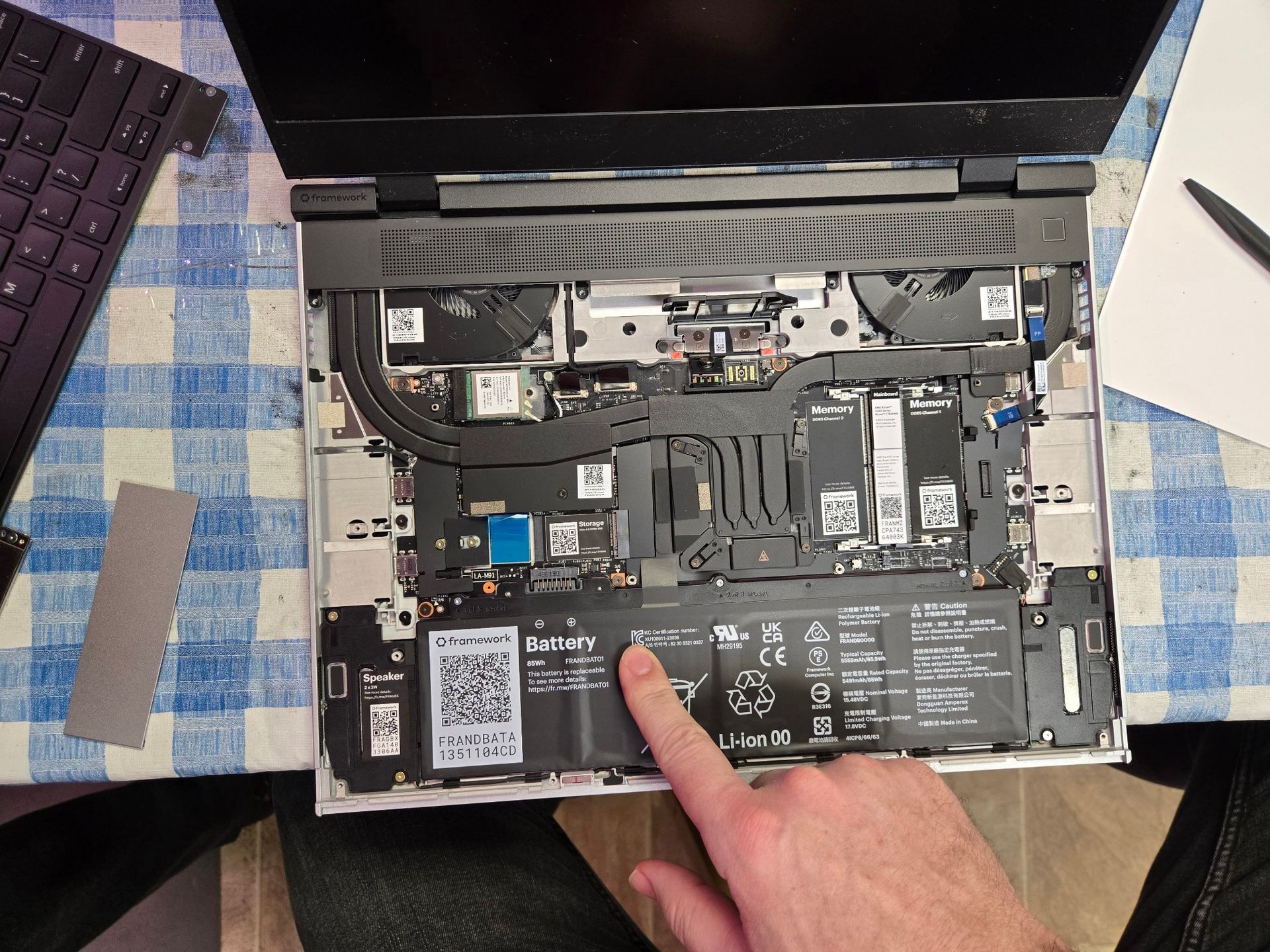 A person is pointing at the battery of a laptop computer.