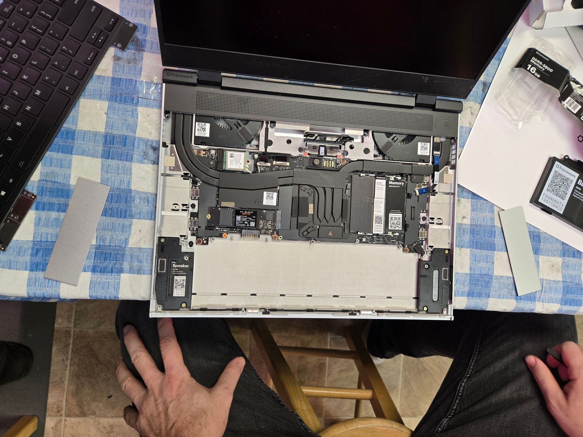 A person is taking apart a laptop on a checkered table cloth.