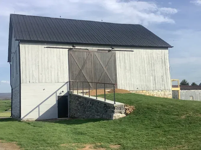 A gray painted wooden bank barn with black door and black roof.