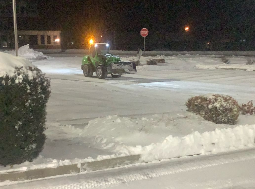 Person in a blue coat clearing a snowy driveway with a snowblower.