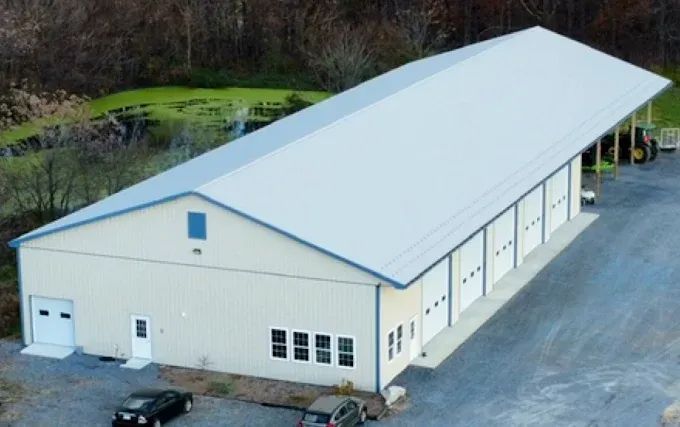 Large white metal warehouse with a blue roof, multiple garage doors, and gravel lot.