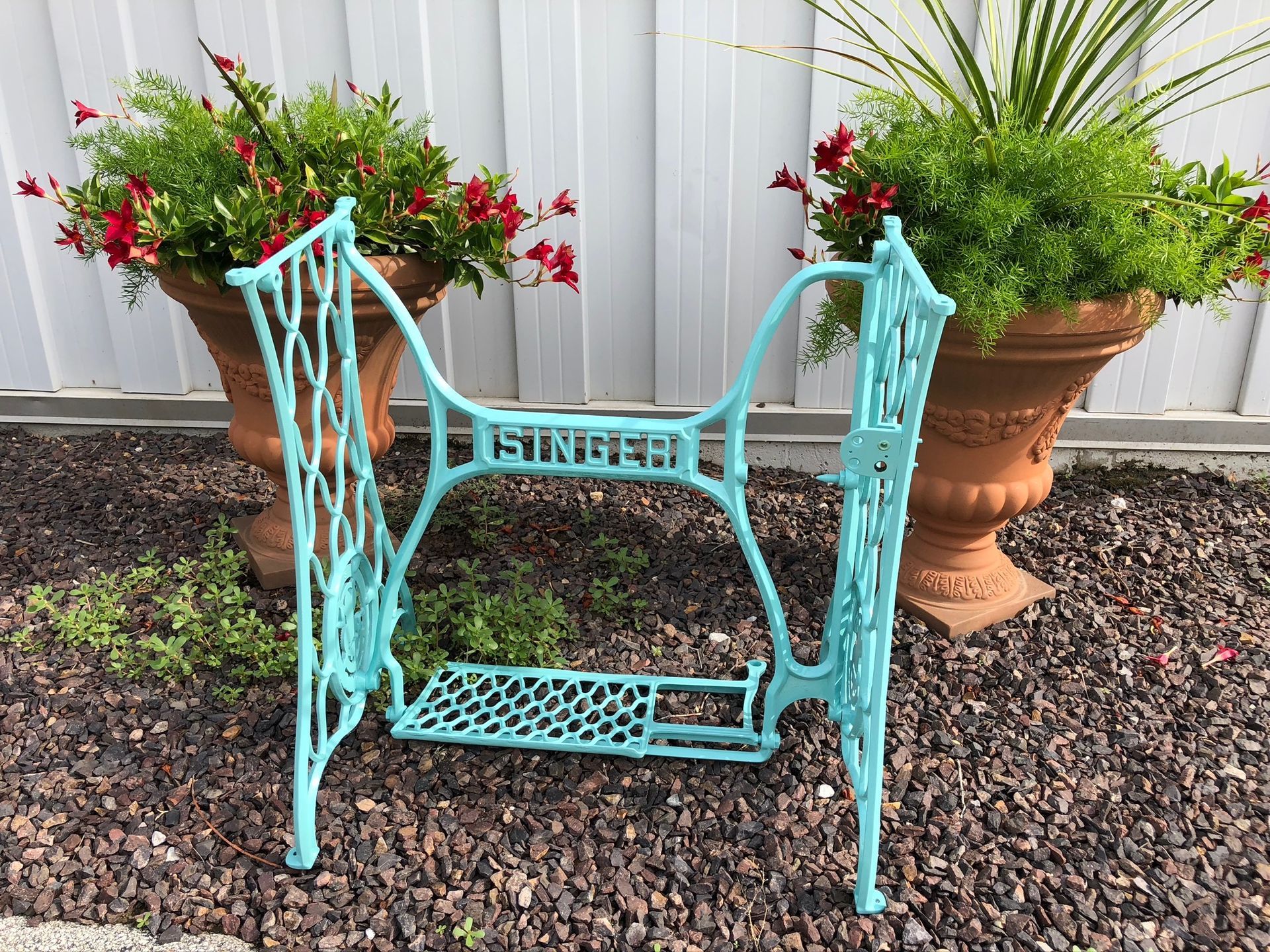 A blue singer sewing machine is sitting in a gravel area next to potted plants