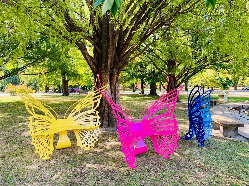 Three butterfly shaped benches are sitting under a tree in a park.