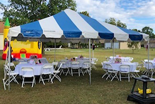 Blue and white striped tent over round tables and white chairs set up on grass.