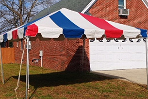 A striped red, white, and blue tent set up in front of a brick building with a garage door.