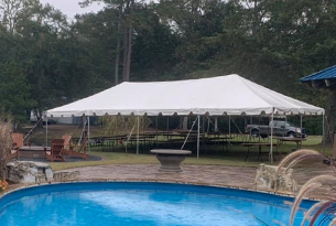 White tent set up outdoors near a pool with tables underneath; a vehicle is visible in the background.