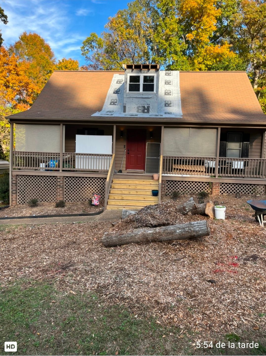 Small brick house with a red door, front porch, and autumn trees in the background.