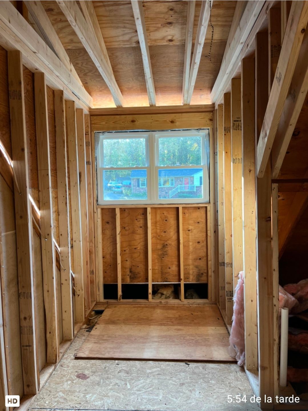 Unfinished wooden room framing with a small window at the far end and exposed studs and ceiling beams.