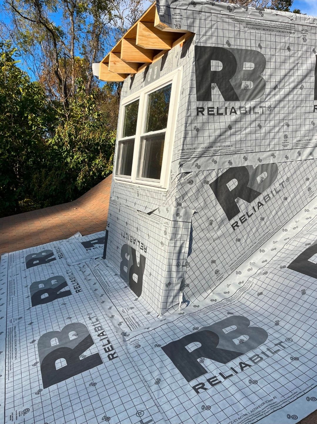 Partially built house wrapped in white RELIANCE sheathing, with a window and roof overhang outdoors