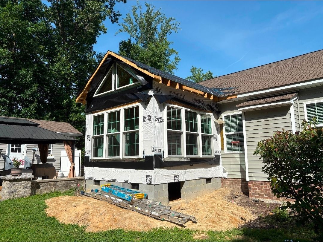 House exterior with a white sunroom addition under construction, surrounded by dirt and materials.