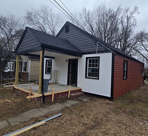 Small house under construction with white siding, red siding, and a covered front porch.