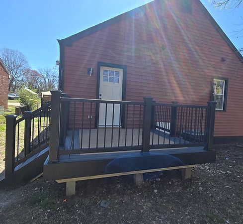 Red brick house with a small front porch and black railing in bright sunlight