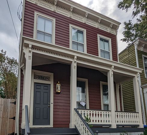 Two-story red house with white trim, dark gray door, and front porch on a tree-lined street
