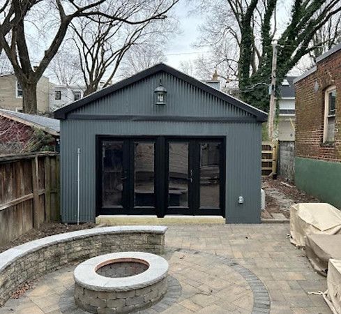 Backyard patio with circular fire pit facing a gray garden building with black doors and windows