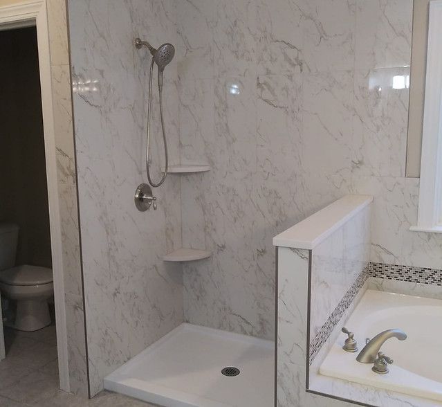 Accessible shower with handheld showerhead, fold-down seat, grab bar, and adjacent sink in a tiled bathroom