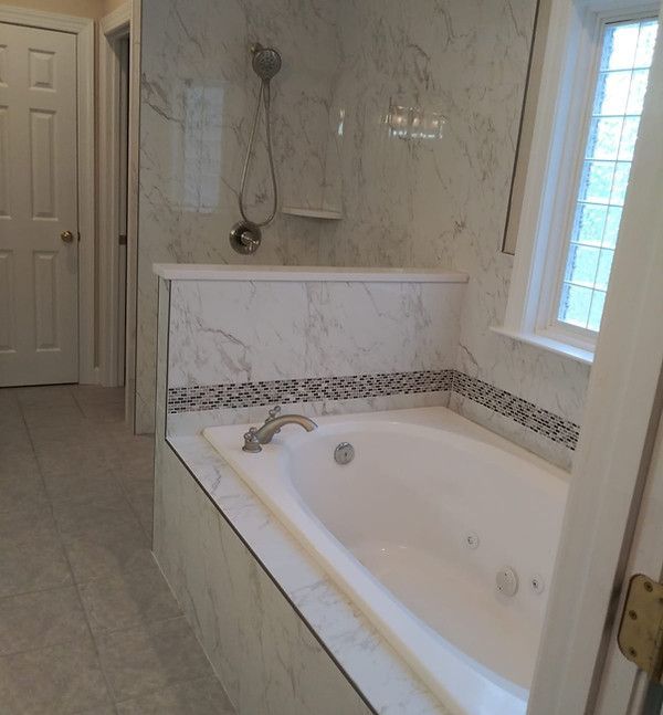 Marble bathroom with a white bathtub, chrome shower fixtures, and a window beside the tub