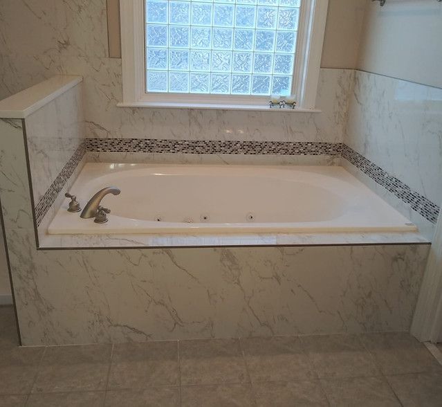 Built-in white bathtub with marble surround beneath a frosted window