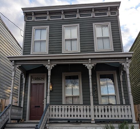 Gray two-story Victorian house with a front porch, white trim, and a red door