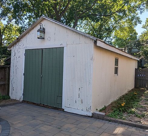 White garden shed with green double doors and side window on a paved backyard patio.