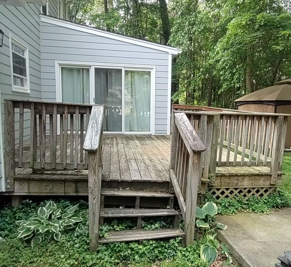 Wooden deck steps leading to sliding glass doors on a gray house, surrounded by green trees.