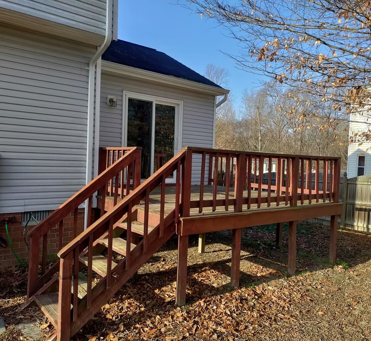 Wooden deck and stairs attached to a house, with white siding and autumn leaves below.