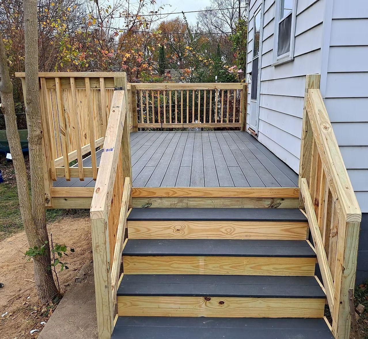 Wooden deck stairs with black treads leading to a gray-sided house and railing-lined porch