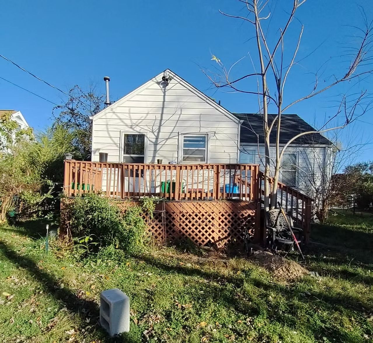 Small white house with a wooden front deck and stairs in a grassy yard under a blue sky