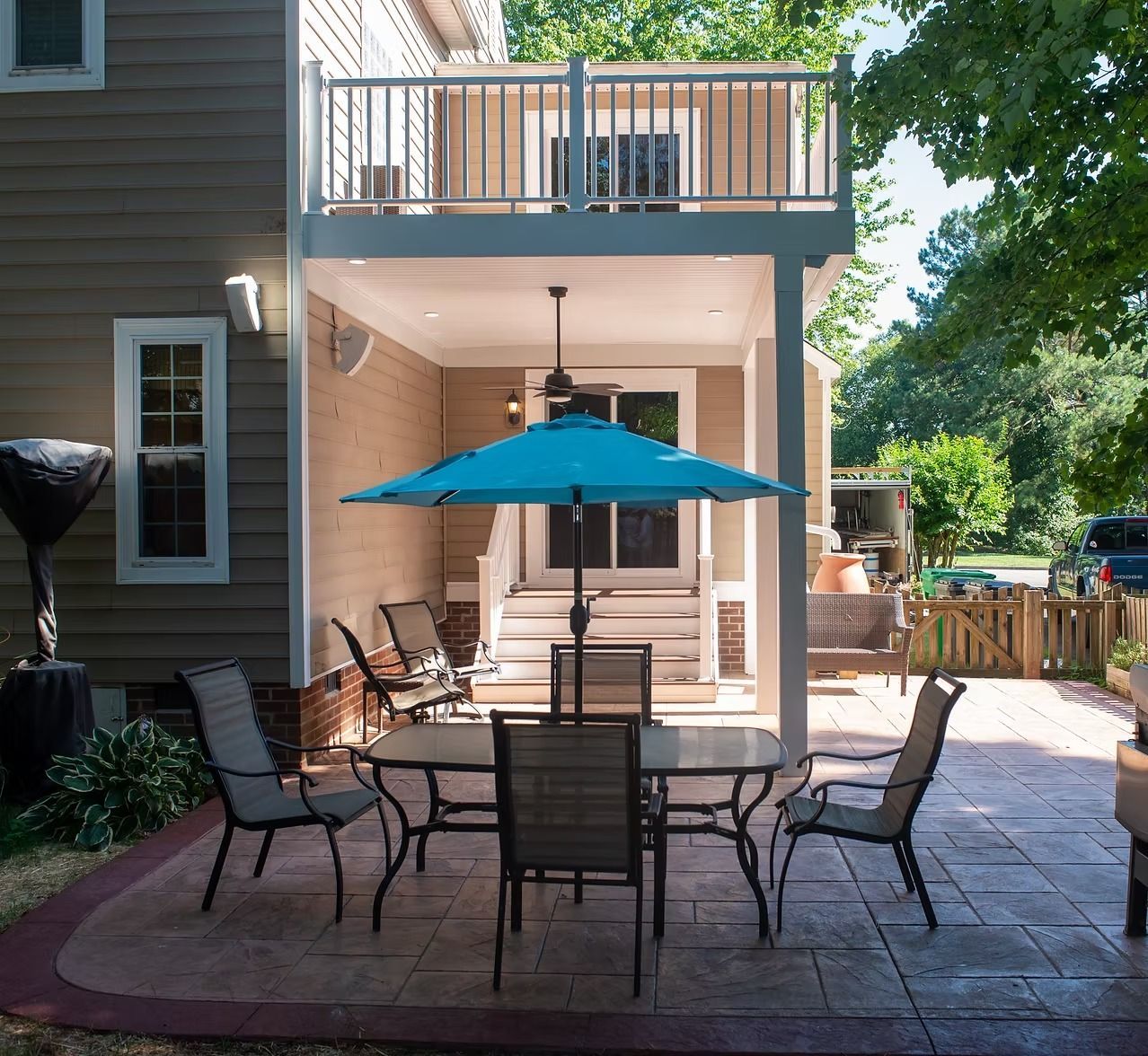 Back patio with dining table, blue umbrella, chairs, and covered porch on a sunny day