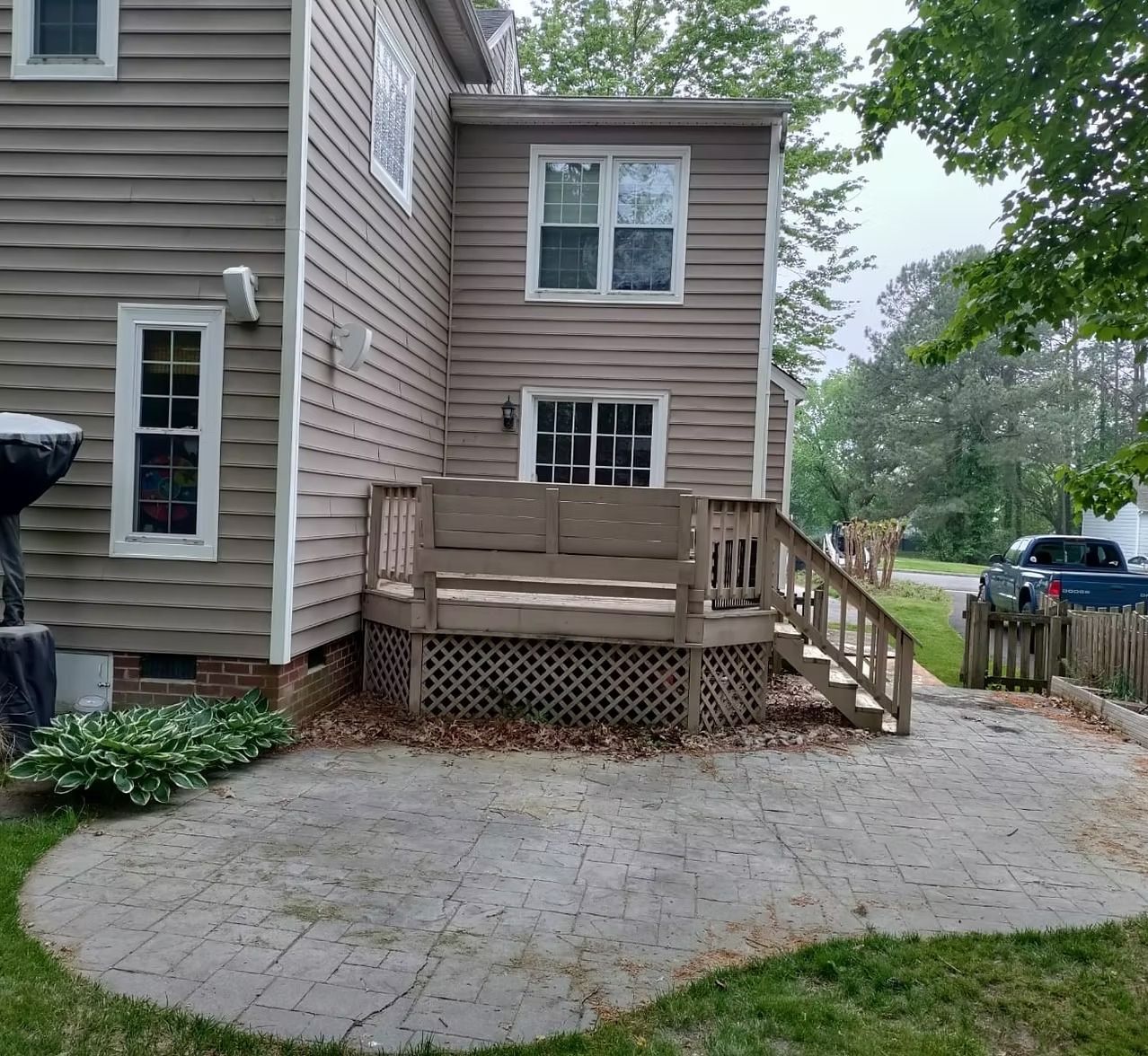 Small house exterior with tan siding, raised wooden porch, stairs, and a paved driveway.