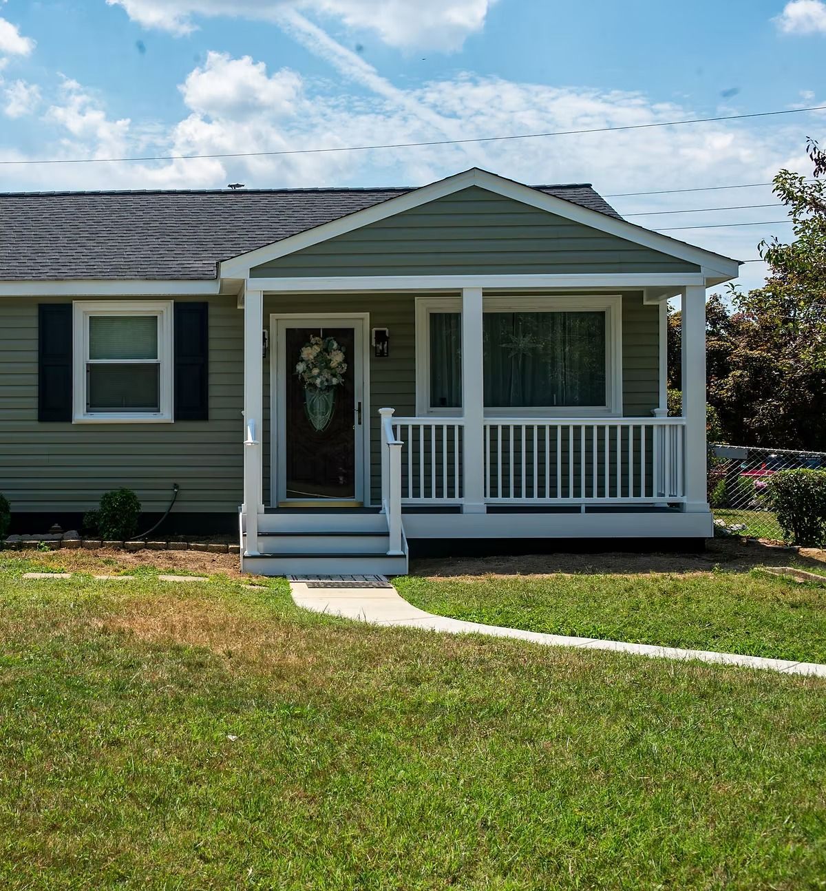 Small house with a covered front porch, white railing, and green lawn under a blue sky