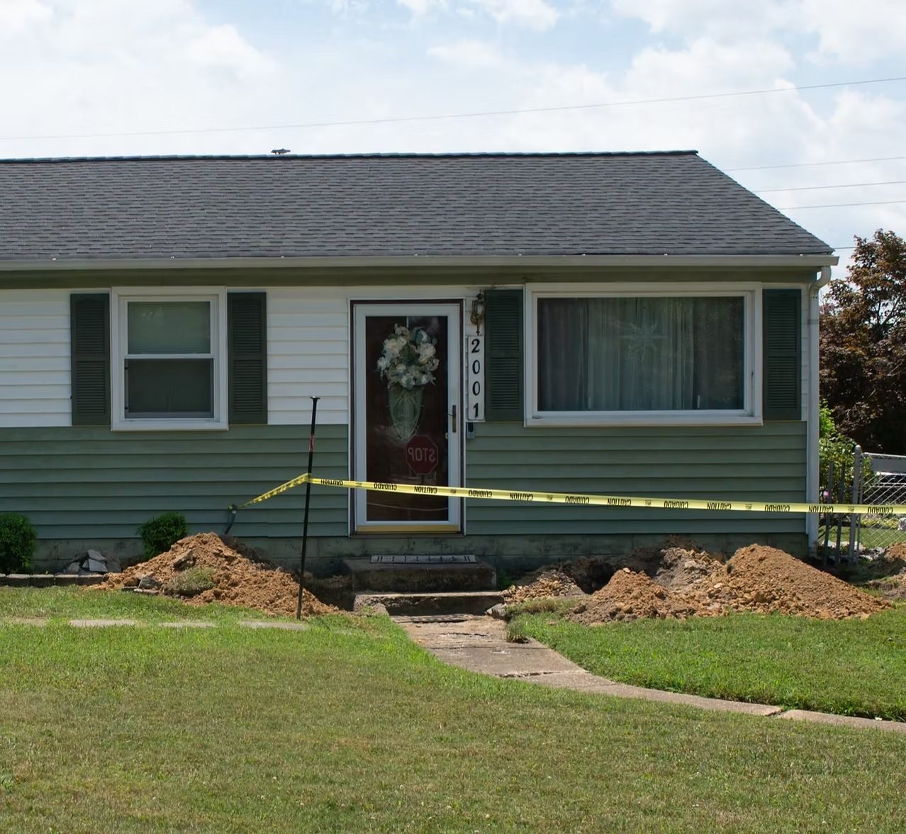 Small house with a front porch under construction, yellow caution tape, and piles of dirt in the yard