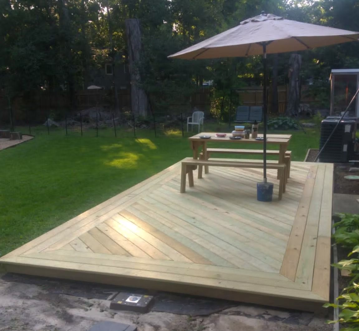 Wooden backyard deck with picnic table, umbrella, and a bucket in sunlight