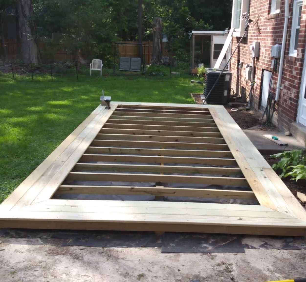 Wooden deck frame under construction in a backyard beside a brick house