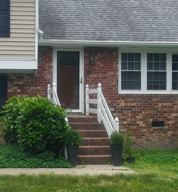 Brick house front entrance with steps, white railing, and a front door beside a window.