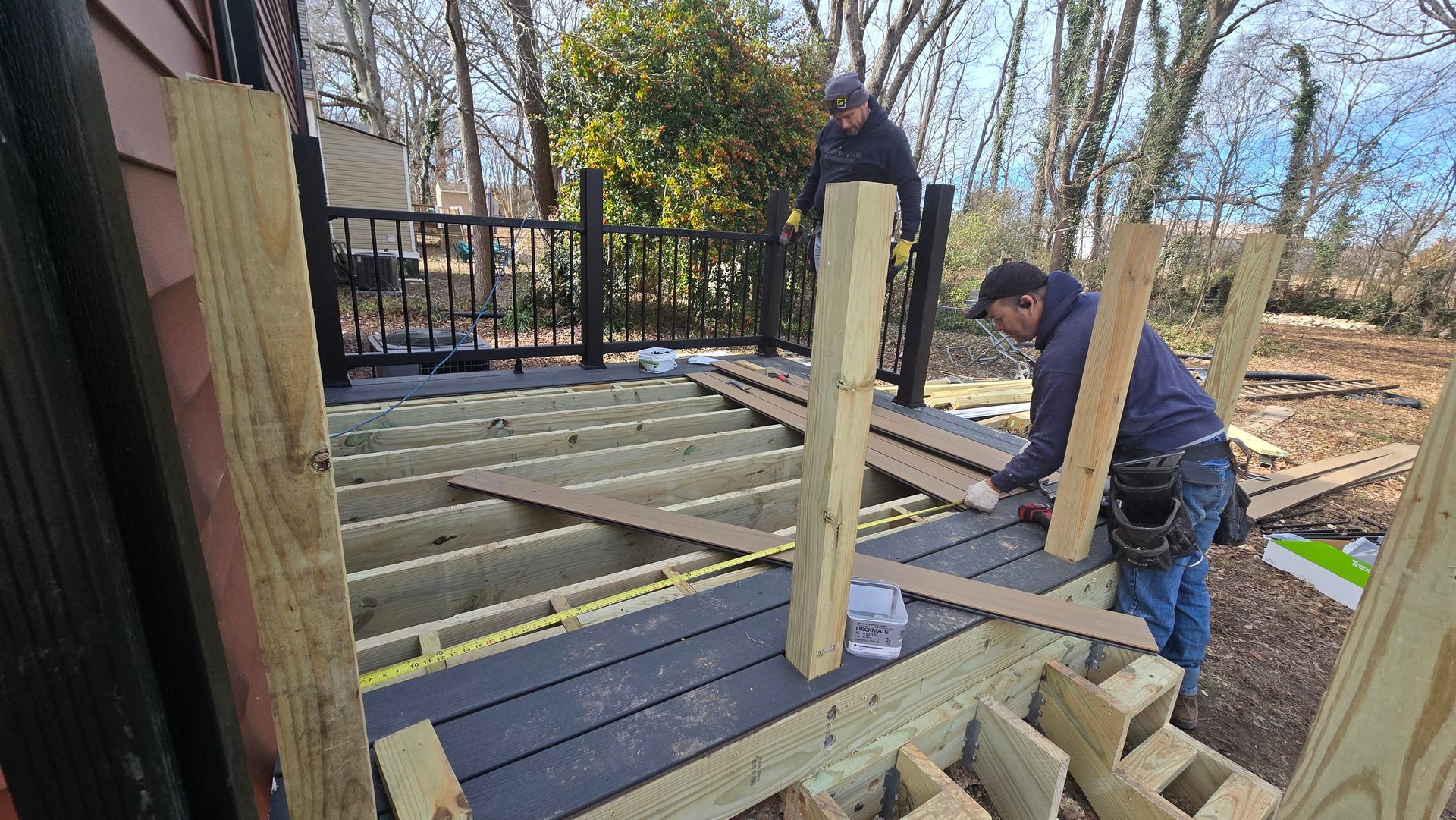 Worker installing joists on a wooden deck frame beside a black metal fence