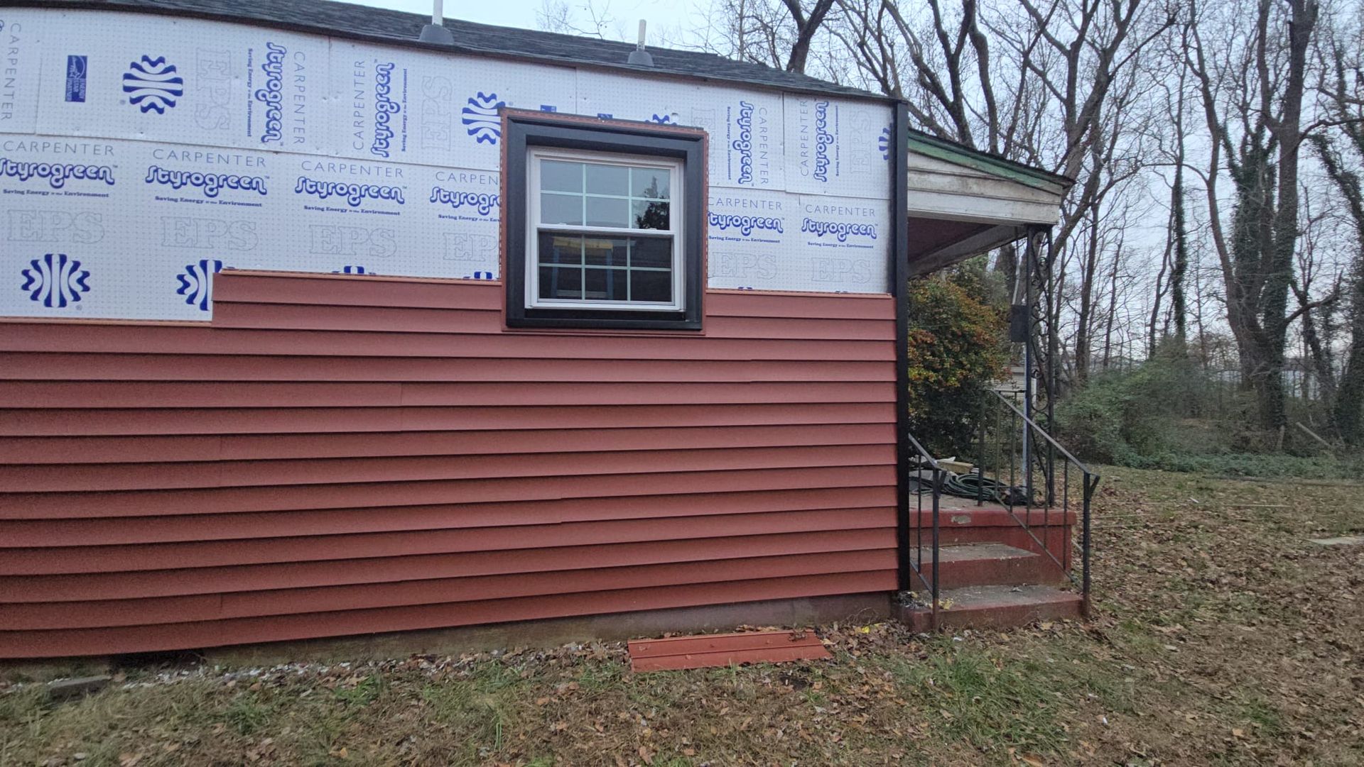 Partially renovated house exterior with red siding, window, and exposed wrap along the roofline