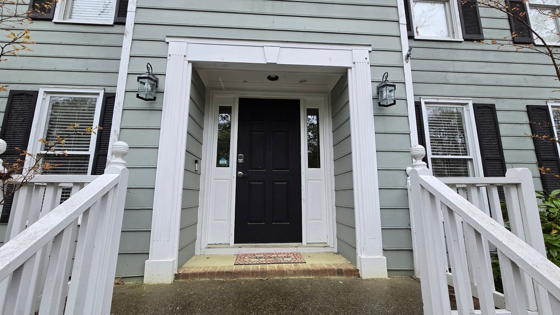 Front entrance of a gray house with white trim, black door, and steps with white railings.