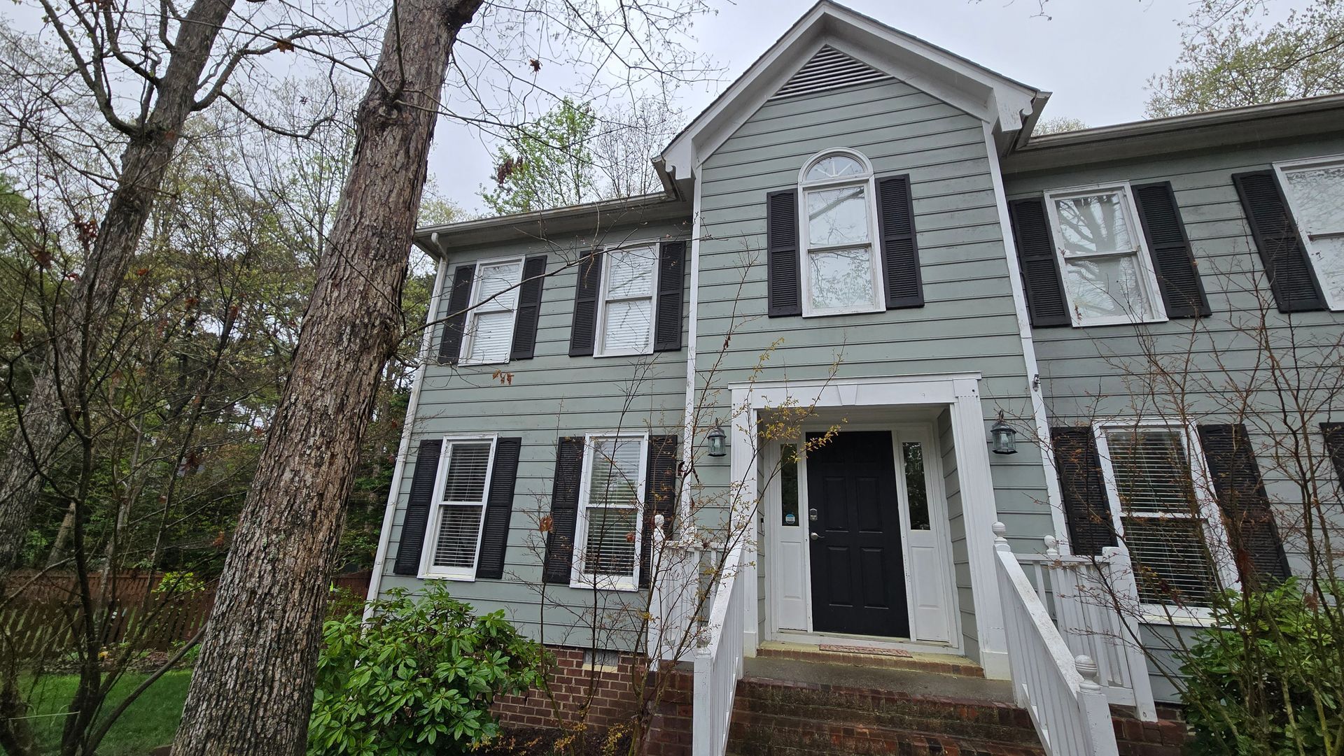 Gray two-story house with white trim, black shutters, and a front porch amid bare trees