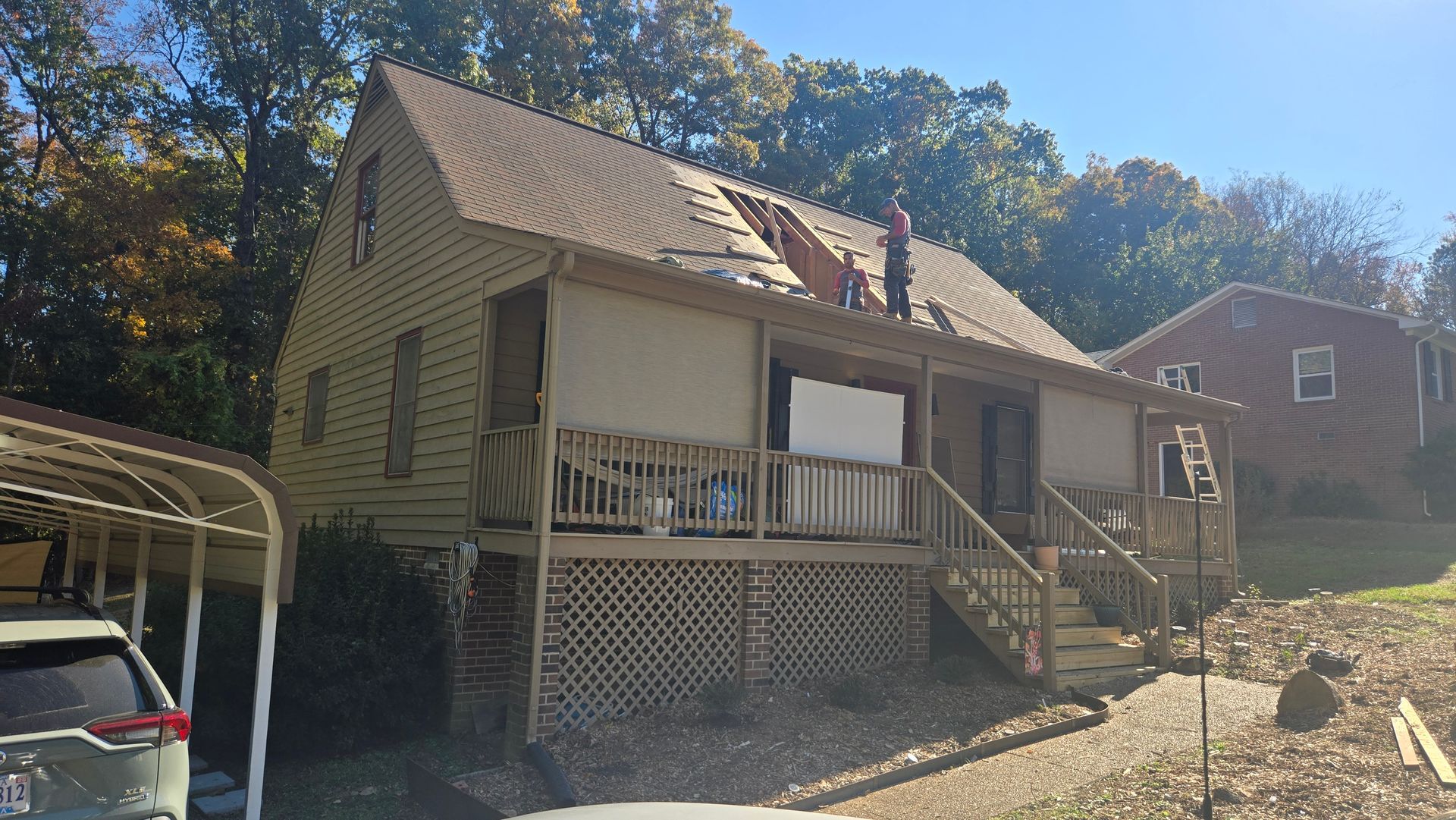 Two-story beige house with porch and stairs, seen in sunlight with trees in the background