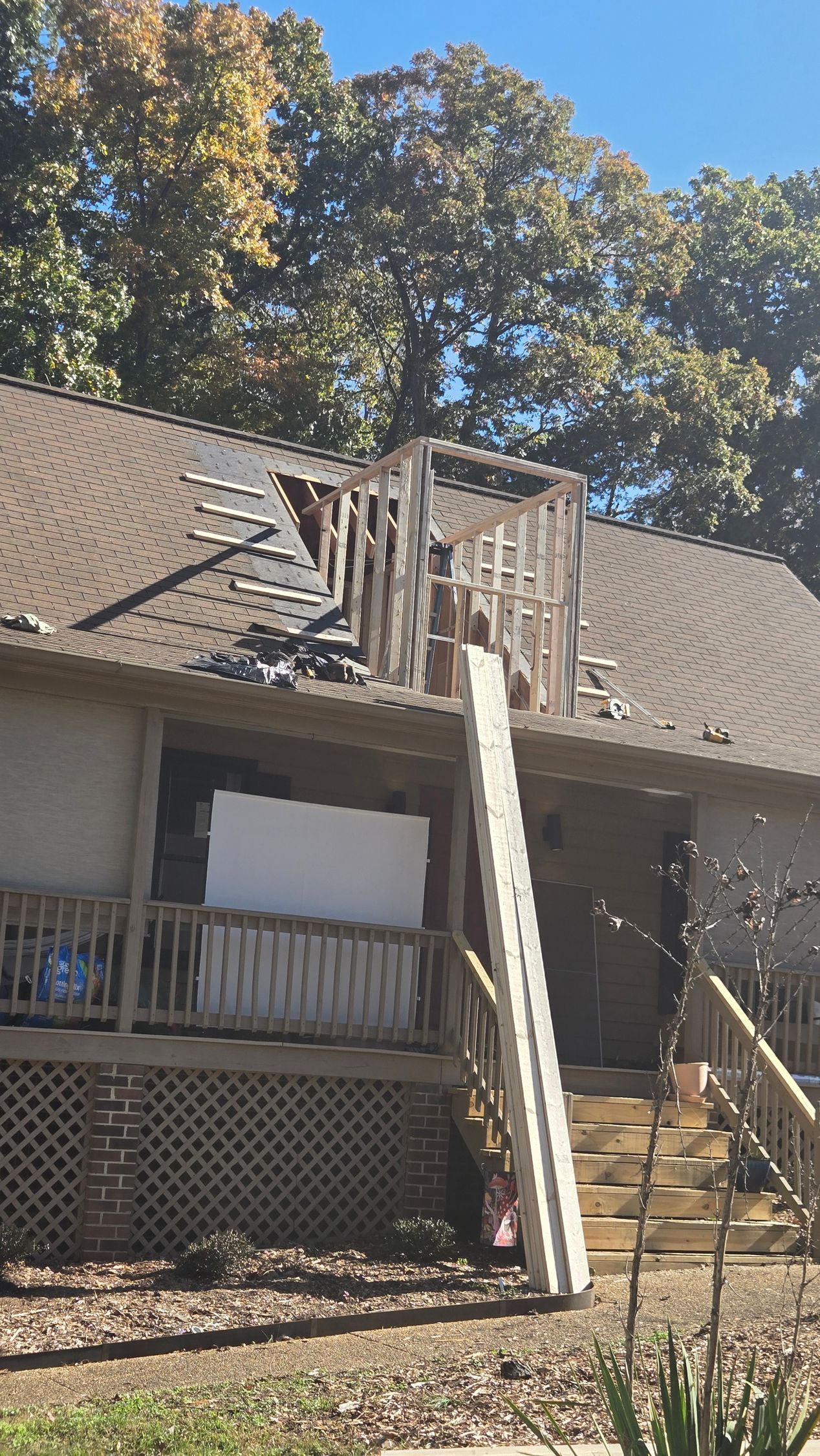 Two-story house with ladder leaning from the ground to a damaged roof deck under trees.