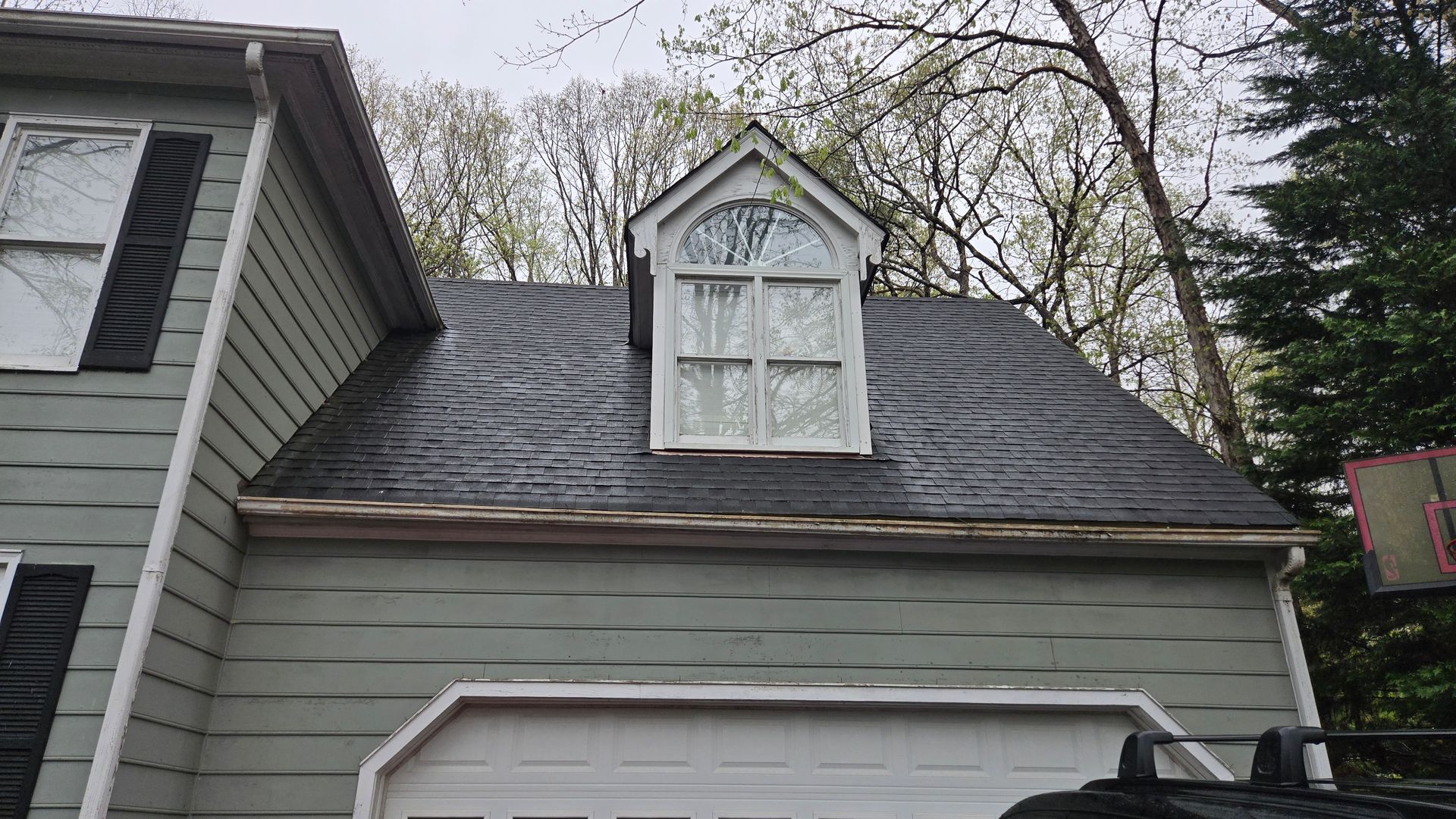 Gray house roof with a small dormer window under leafless trees