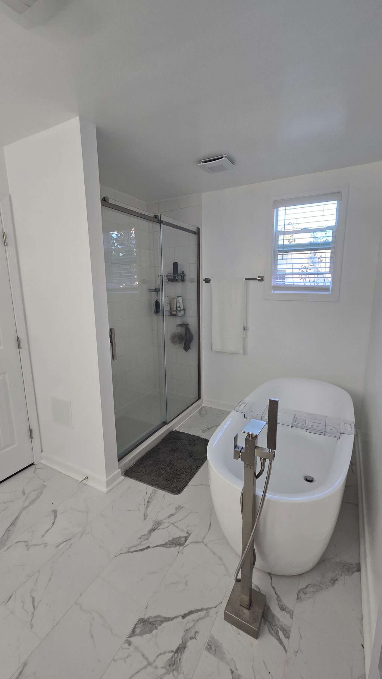 Modern white bathroom with a bathtub, glass shower, and marble tile floor