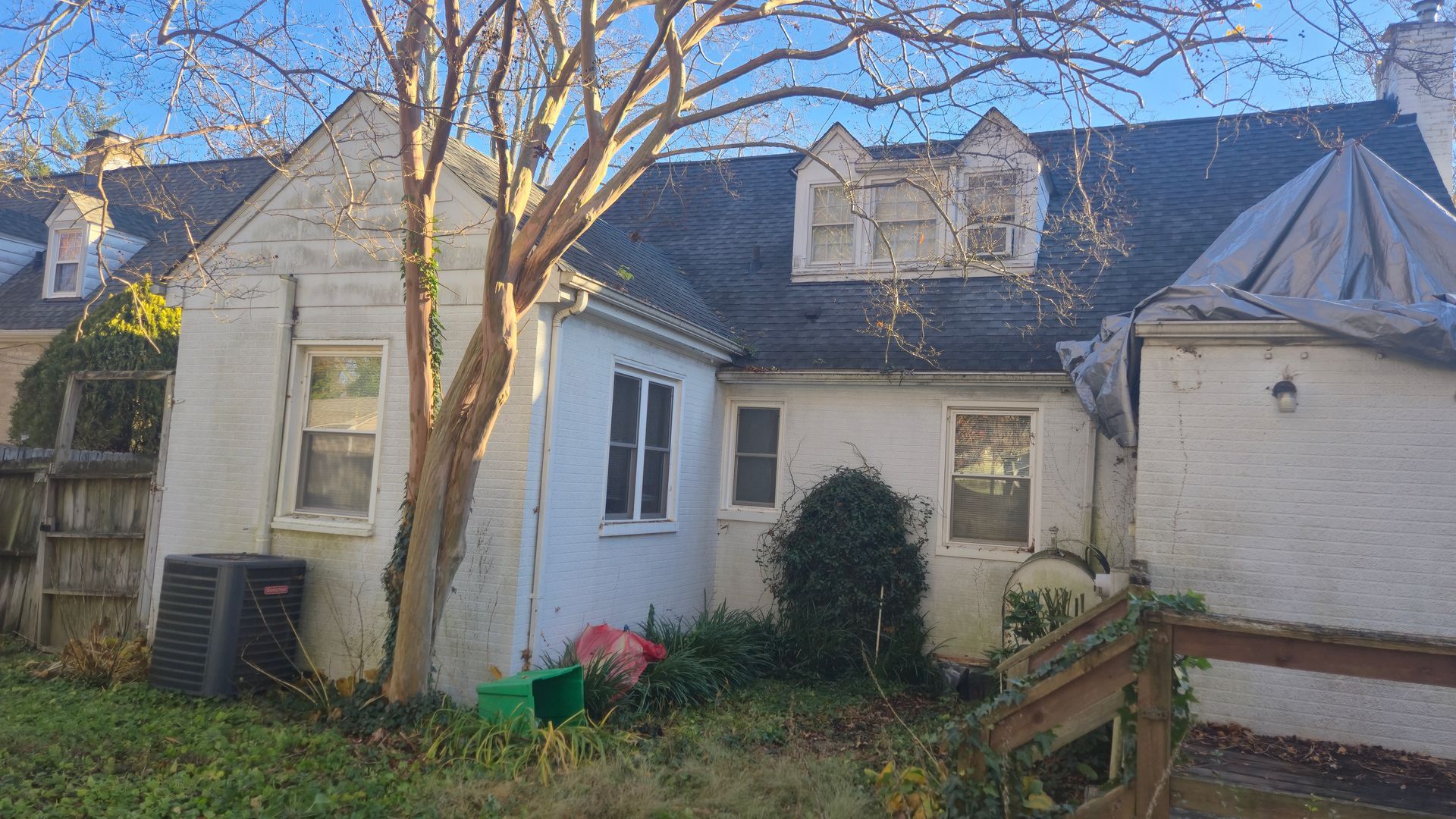 Old white house with a bare tree in the yard and an attached garage on the right