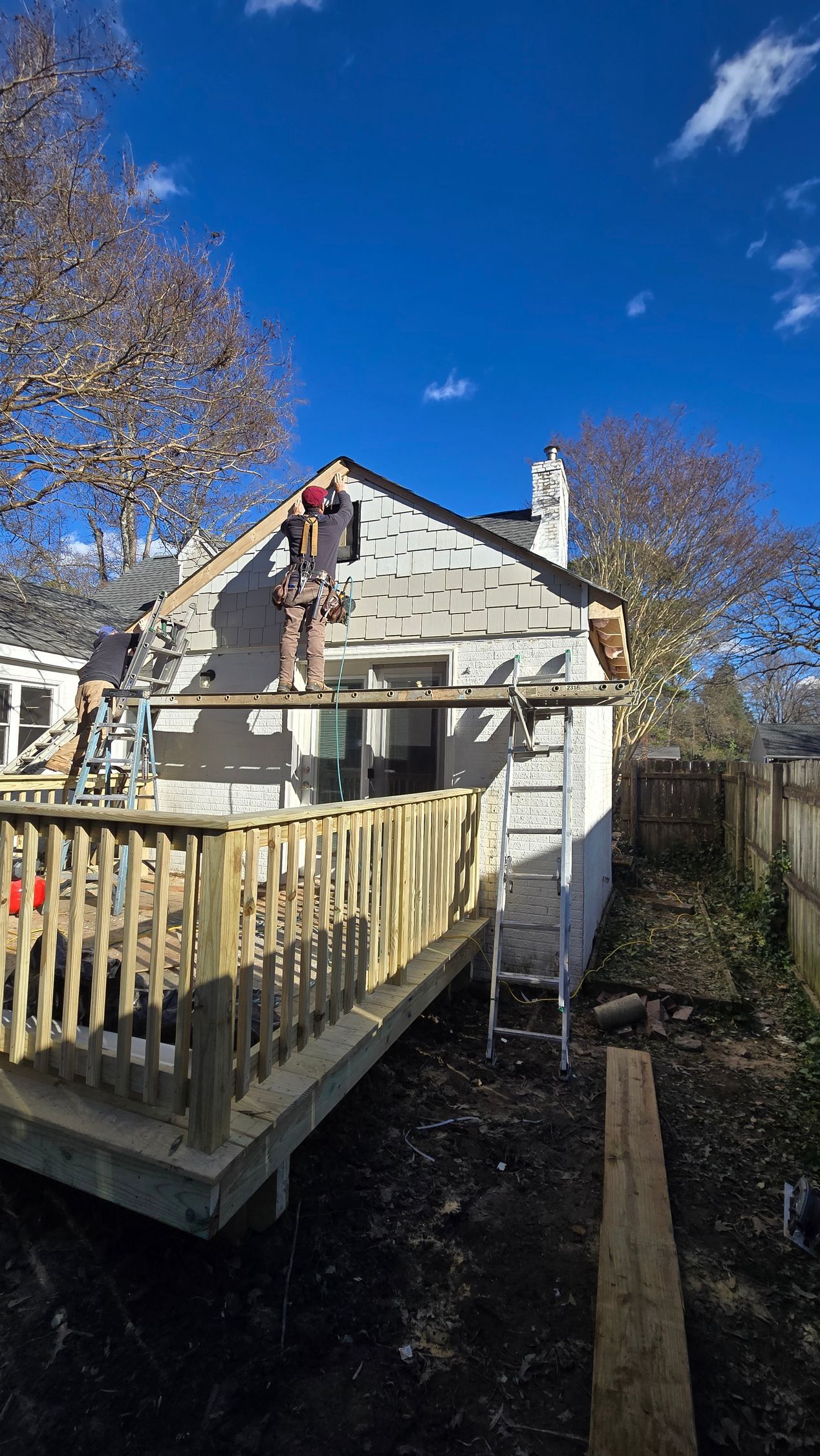 Stone house with a wooden deck and railing under a clear blue sky, with bare trees nearby