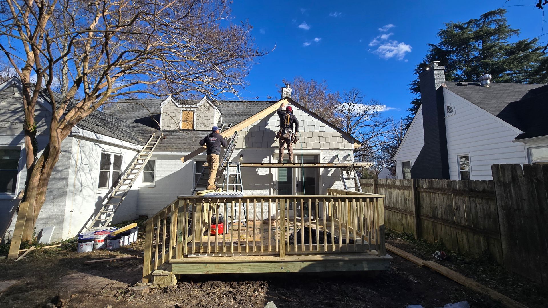 Backyard deck with two workers on a house roof under a clear blue sky