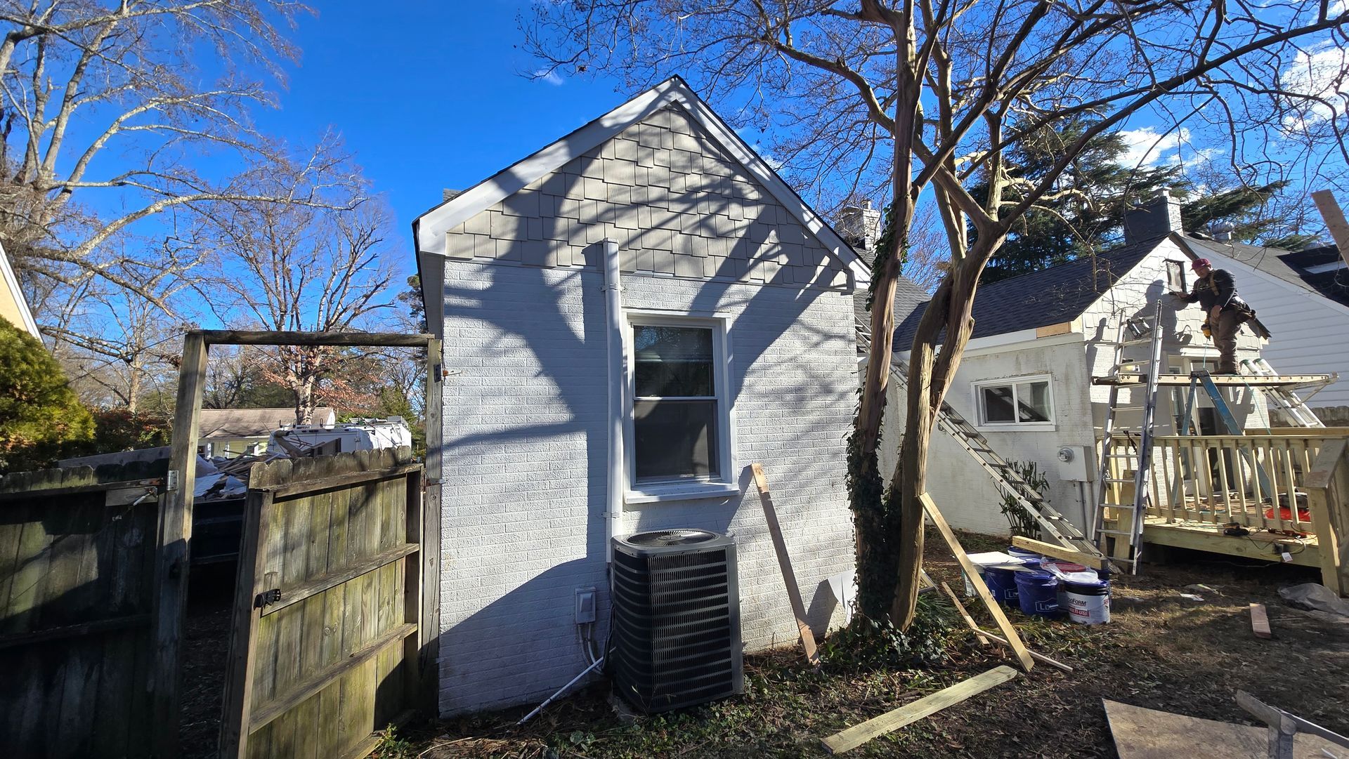 Small white house or shed in a backyard, with a wooden fence, trees, and a blue sky.